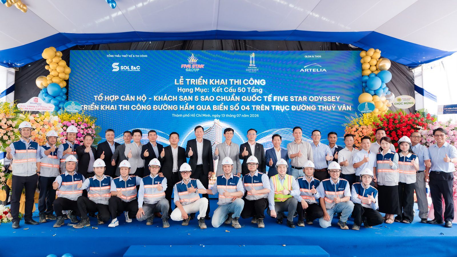 Lễ triển khai thi công kết cấu 50 tầng Five Star Odyssey và hầm đi bộ số 4 ngày 13/7/2026: đội ngũ tổng thầu Sol E&C đội mũ bảo hộ đứng trước backdrop ghi tên hạng mục
